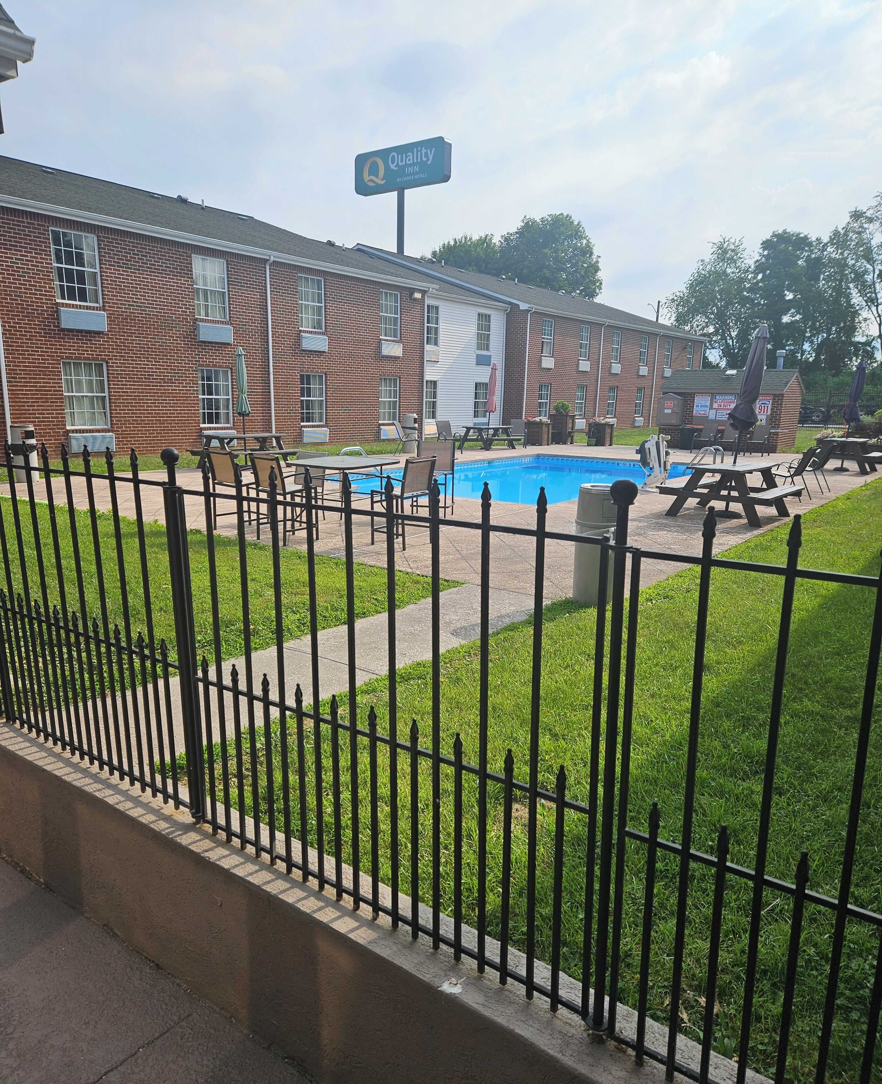 Un bâtiment en briques avec une enseigne « Quality Inn », une piscine, des chaises longues et un patio clos.