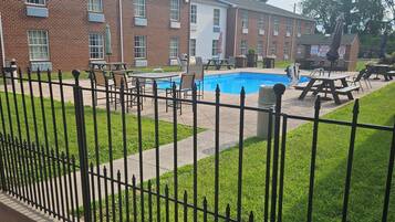 A brick building with a sign for Quality Inn, a swimming pool, lounge chairs, and a fenced patio area.
