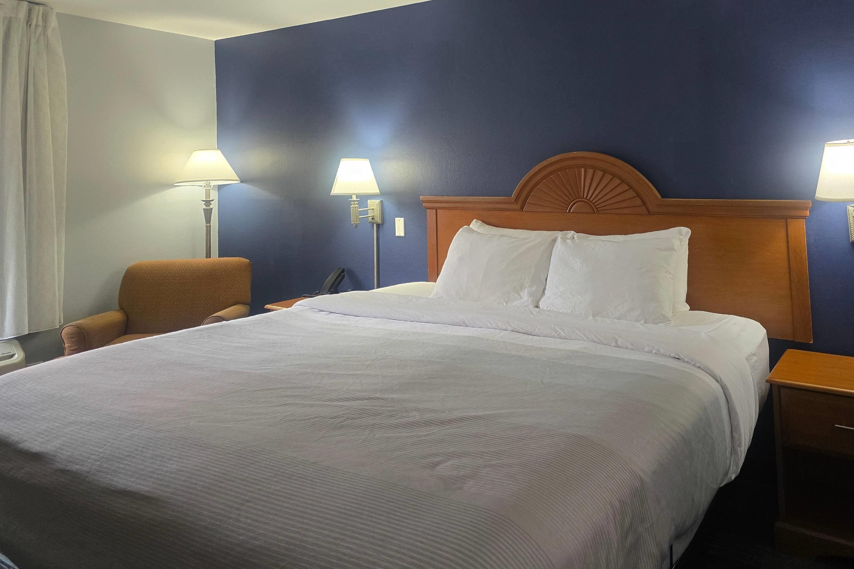 Een hotelkamer met een groot bed, twee bedlampjes, een houten hoofdeinde en een stoel.