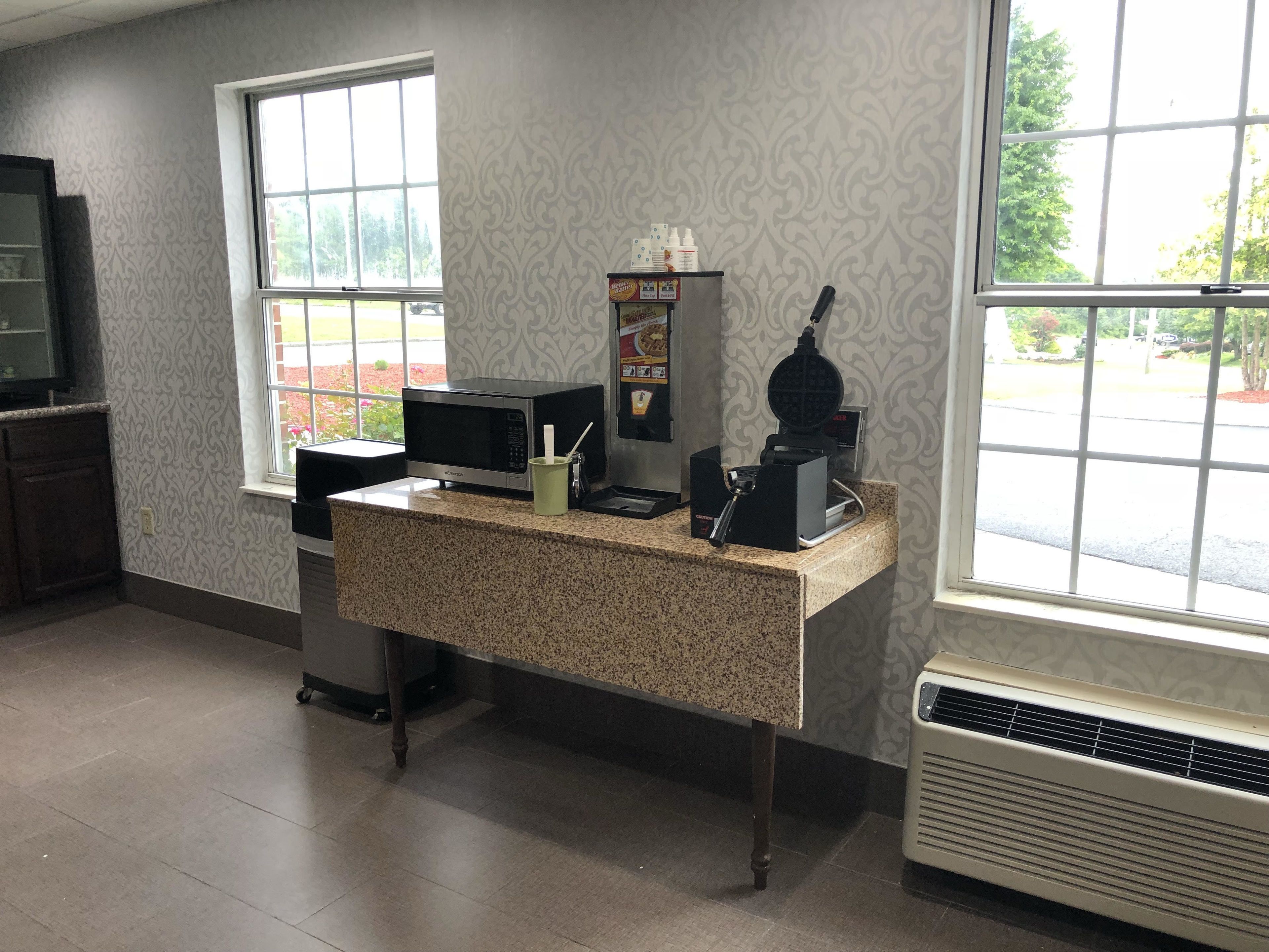 A kitchen with a granite countertop, a microwave, a waffle maker, and a coffee machine.