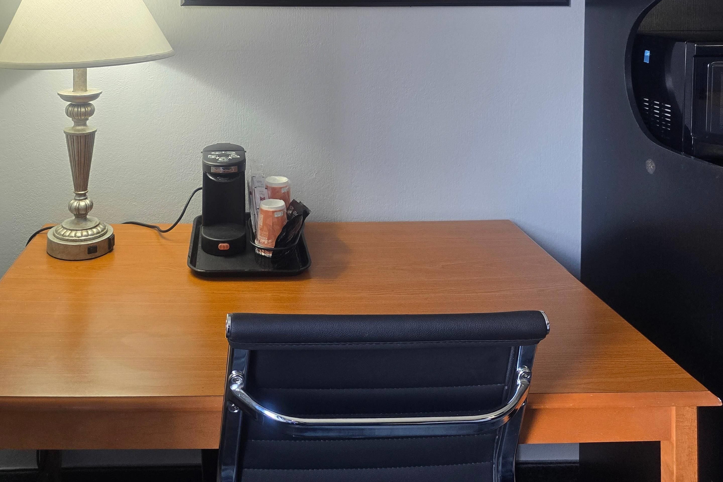 Une table en bois, avec une machine à café, une lampe et une chaise noire.