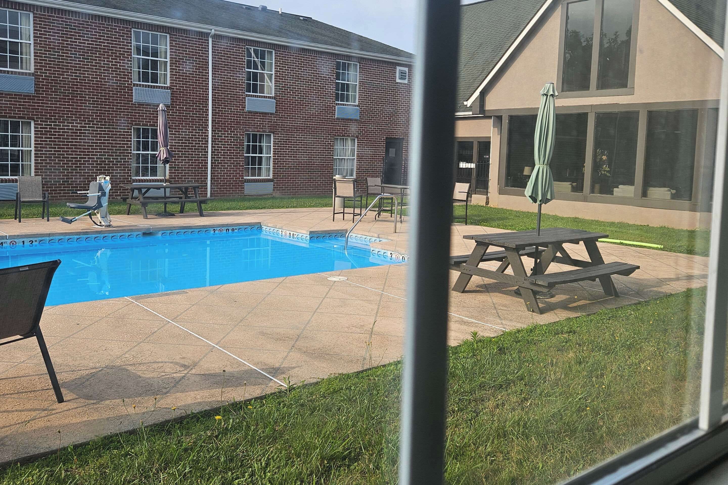 A swimming pool with a brick building in the background, a picnic table, and outdoor seating.