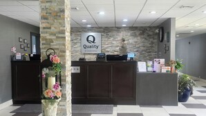 A hotel reception area with a stone pillar, a reception desk, and a sign that reads "Quality by Choice Hotels".