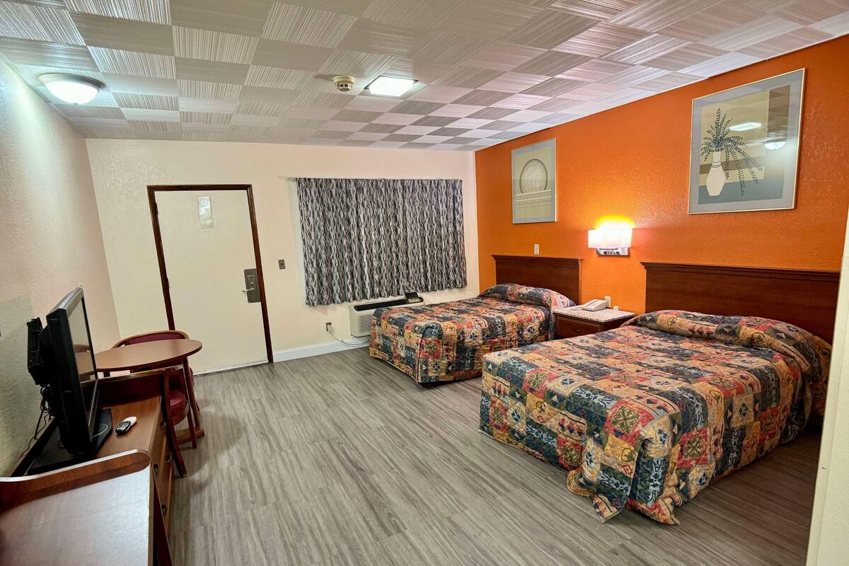 Ein Hotelzimmer mit zwei Betten, einem Schreibtisch mit Fernseher, einer Wand-Klimaanlage und einem gemusterten Vorhang.