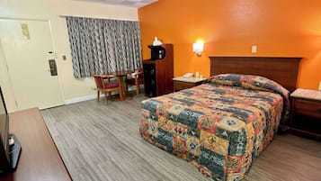 A hotel room with a bed, a desk, a chair, a nightstand, and a lamp.