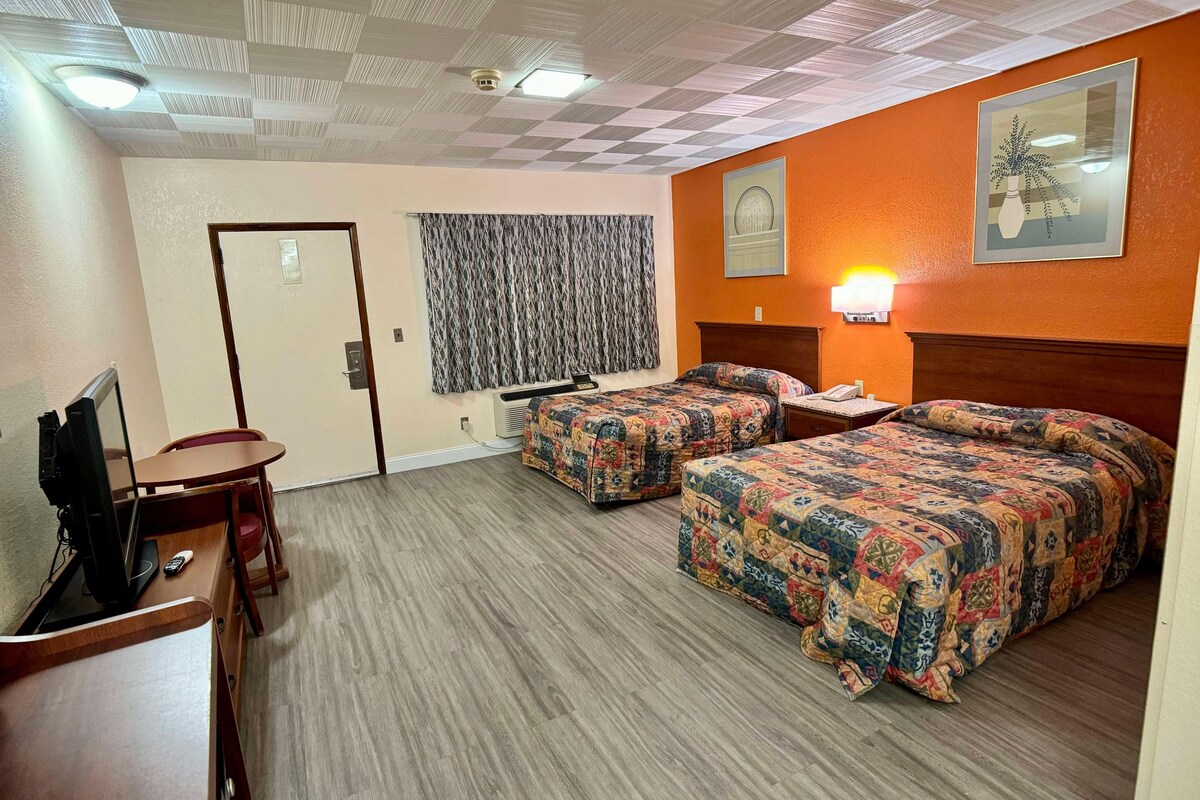 Une chambre d’hôtel avec deux lits, un bureau avec une télévision, un climatiseur fixé au mur et un rideau à motifs.