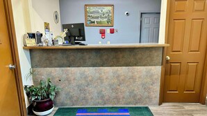 A reception area with a check-in/out sign, a computer, a clock, a security camera, and a door. - Knights Inn Galax (Galax)