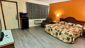 A hotel room with a bed, a desk with a computer, a chair, a microwave, and an air conditioning unit. - Knights Inn Galax (Galax)