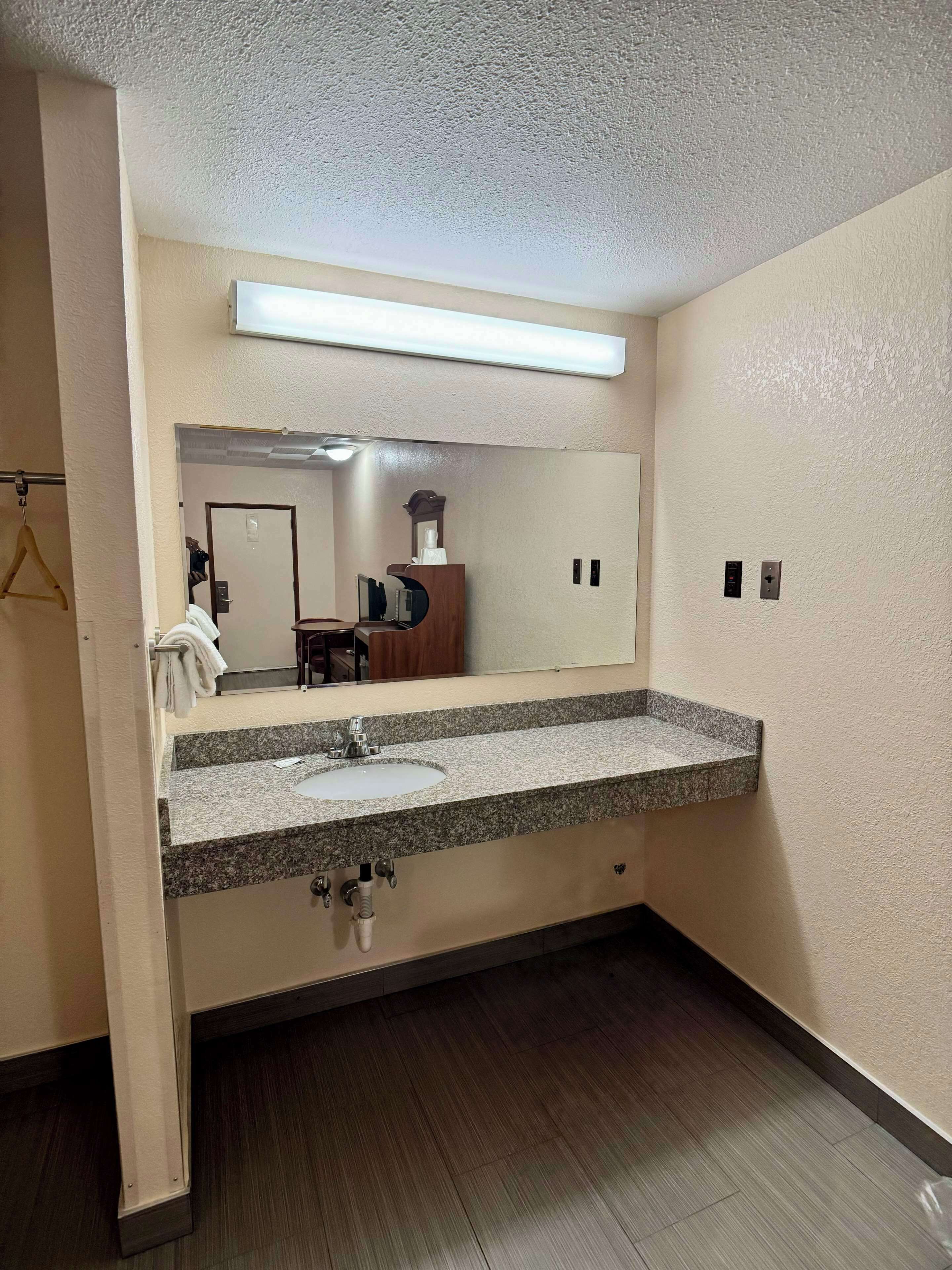 Baño de hotel con lavamanos de encimera de granito, espejo e iluminación en el techo.