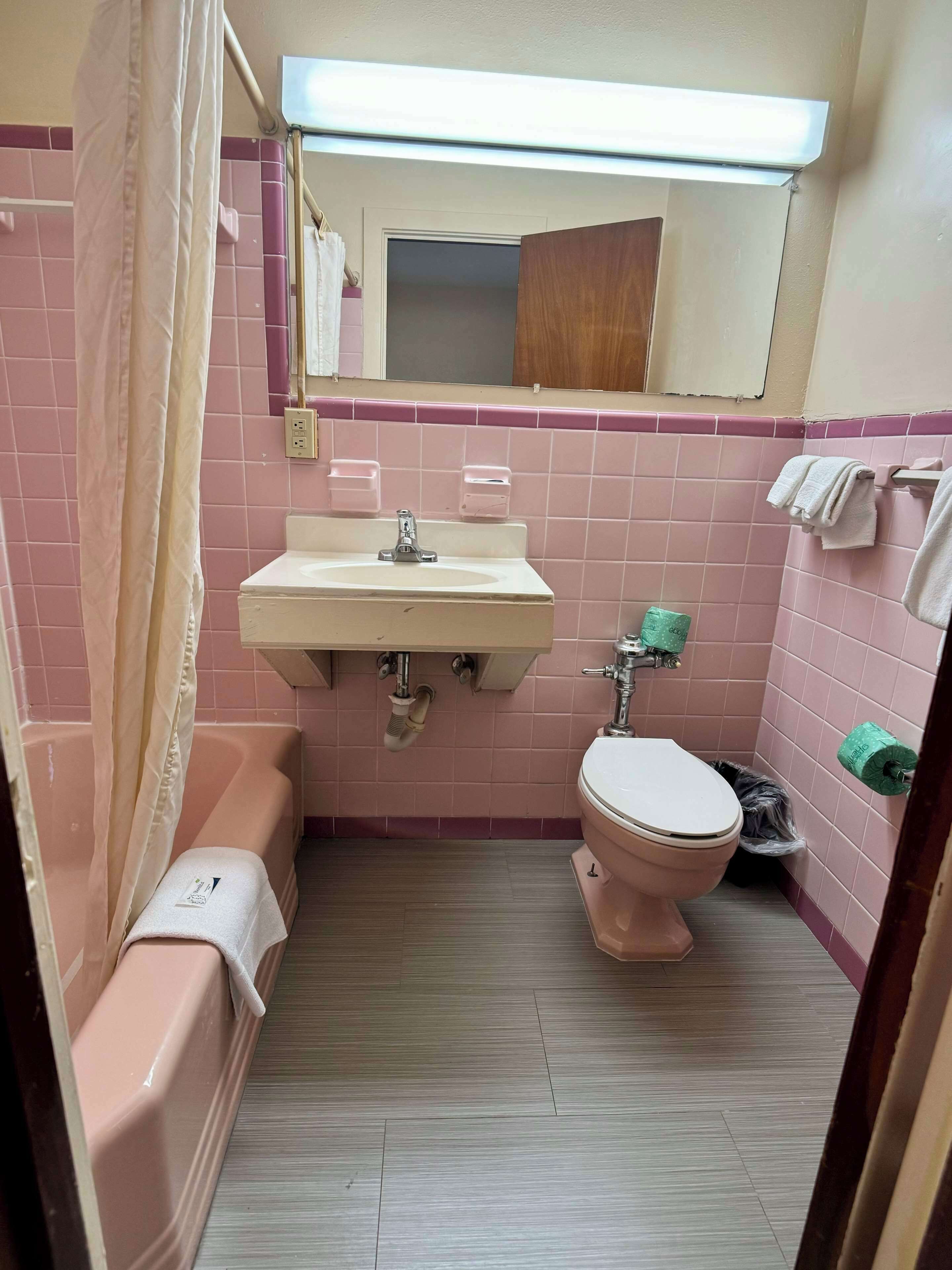 Un baño con azulejos rosas, un lavabo, un inodoro, una bañera y una cortina de ducha.