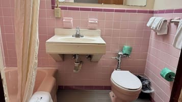 Un baño con azulejos rosas, un lavabo, un inodoro, una bañera y una cortina de ducha.