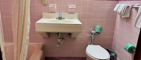 Un baño con azulejos rosas, un lavabo, un inodoro, una bañera y una cortina de ducha.