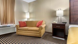 Une chambre d’hôtel avec un sol à rayures, un canapé avec un coussin rouge, une table de chevet avec une lampe et un lit avec une couverture jaune.