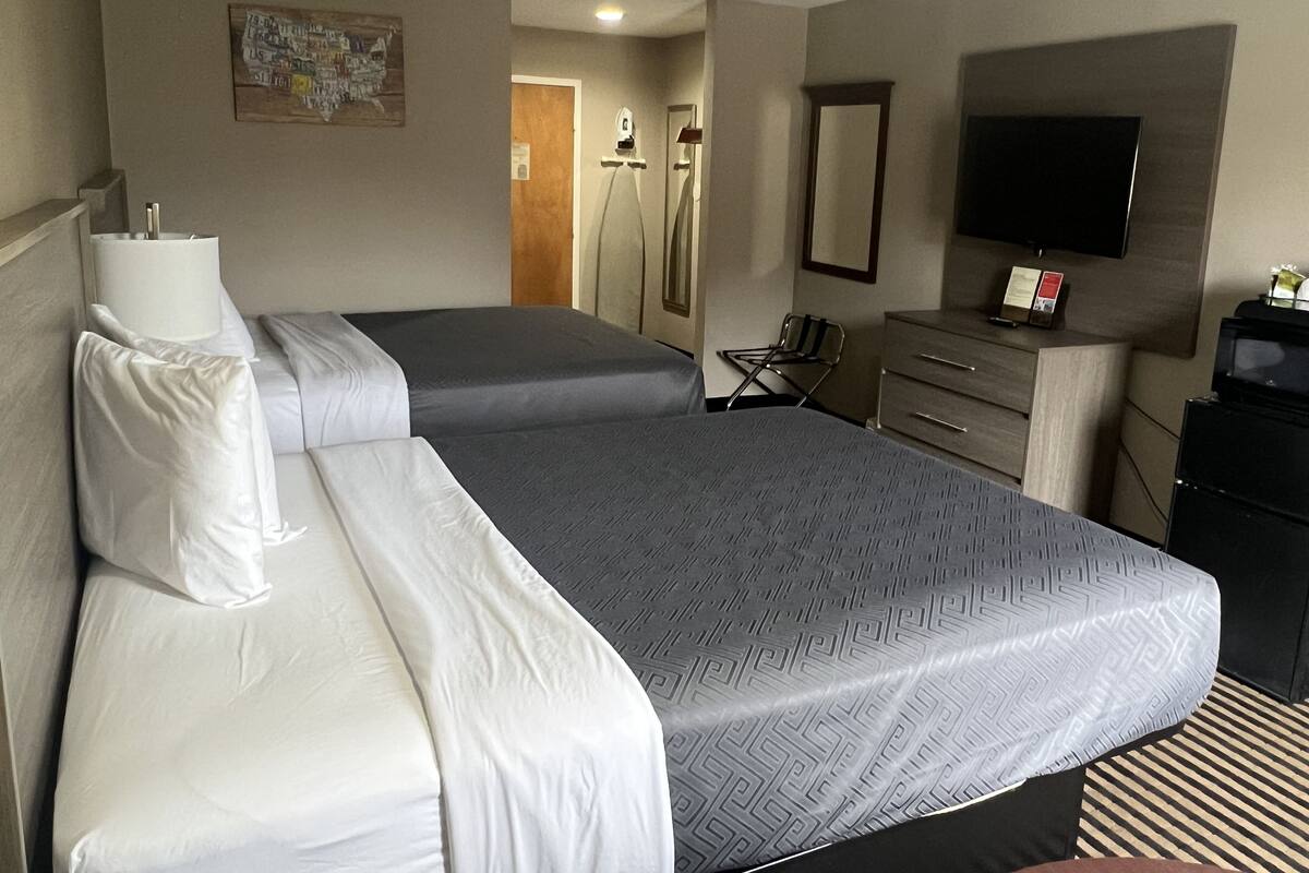 Quarto de hotel com duas camas, uma escrivaninha, uma cadeira, uma televisão e um espelho.