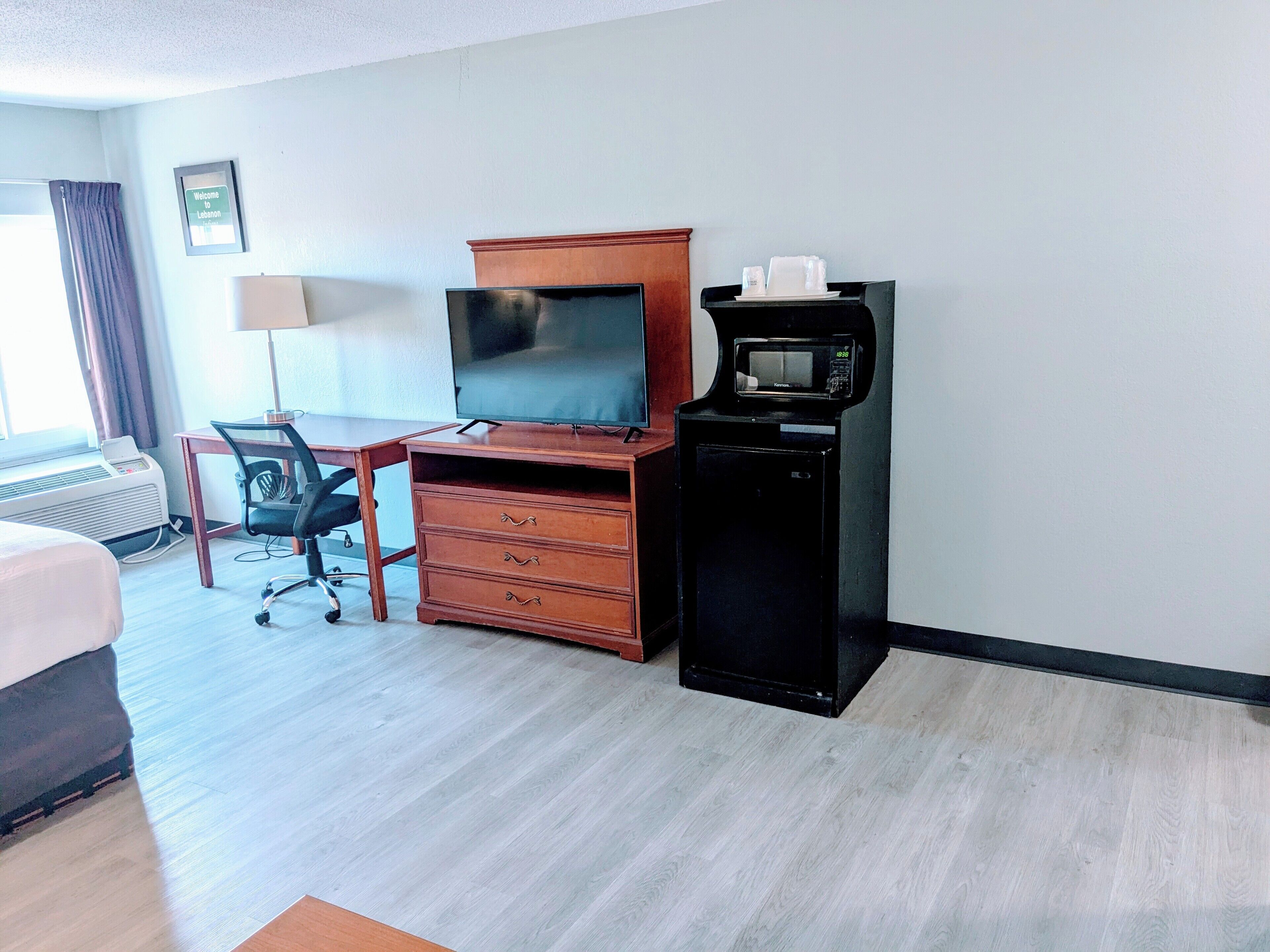 Habitación de hotel con cama, escritorio con computadora, televisor, microondas y refrigerador pequeño.