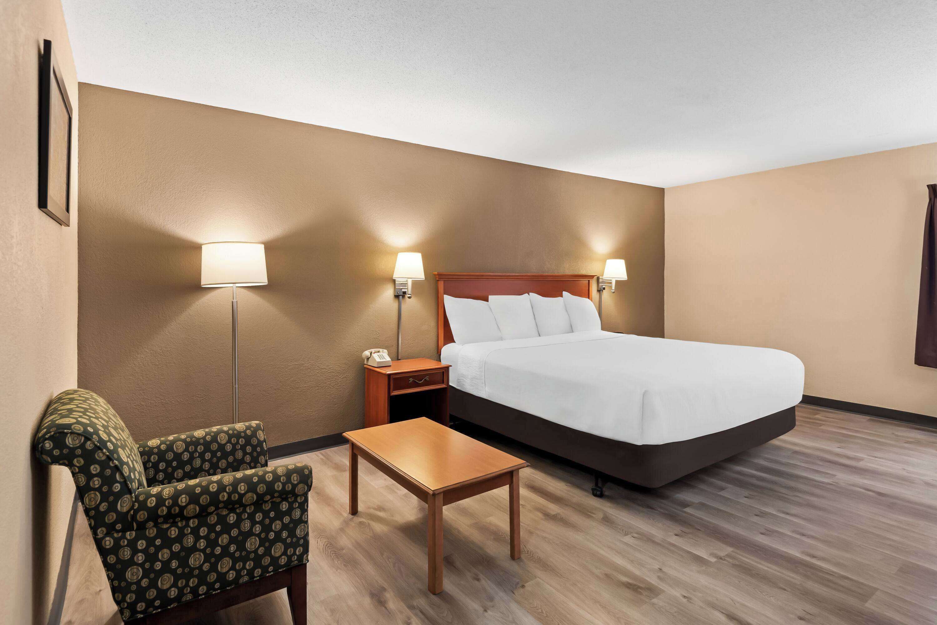 Una habitación de hotel con una cama, una mesita de noche, una silla y una pequeña mesa.