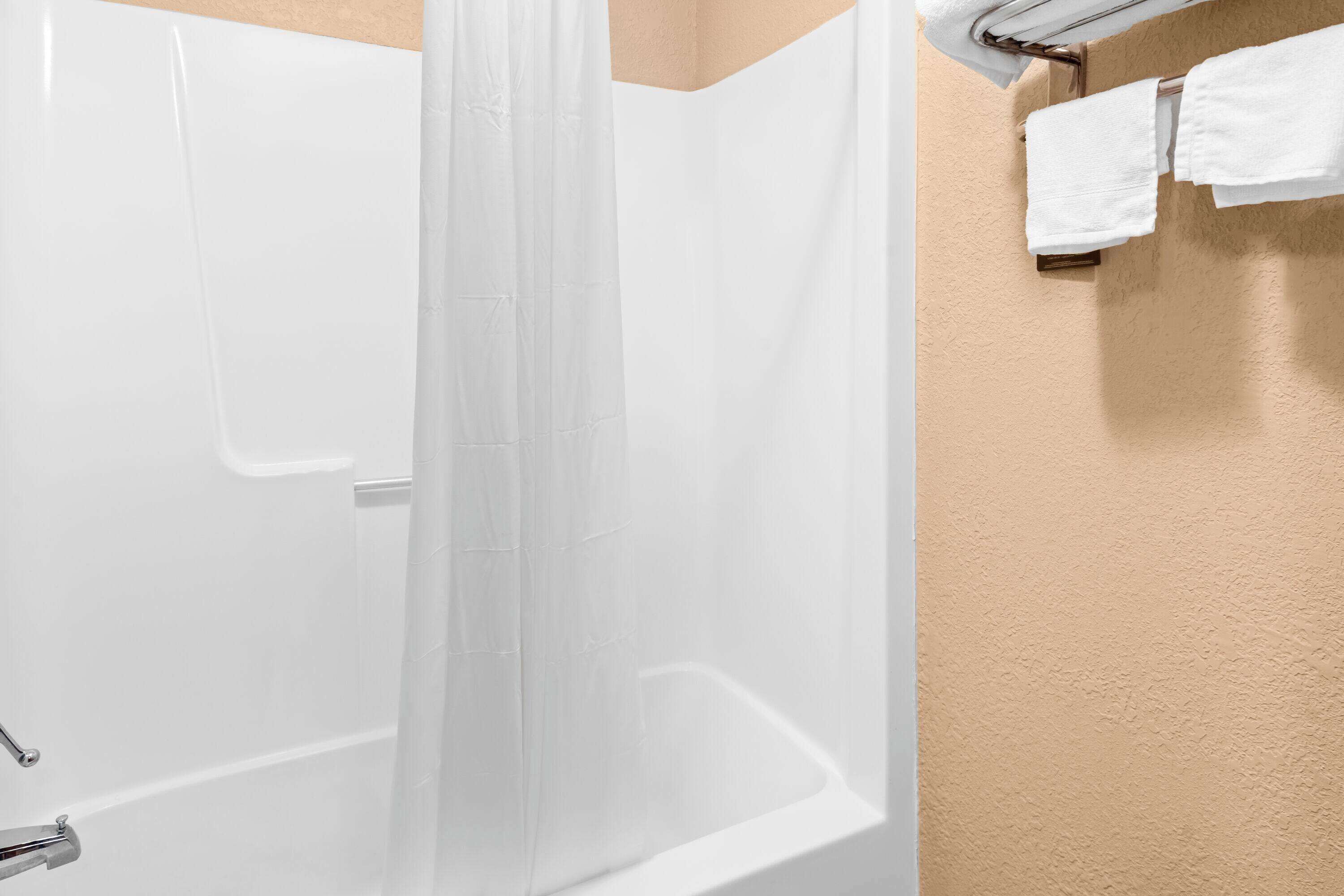 Una zona de ducha con puerta de vidrio, un perchero con dos toallas blancas y una pared color beige.