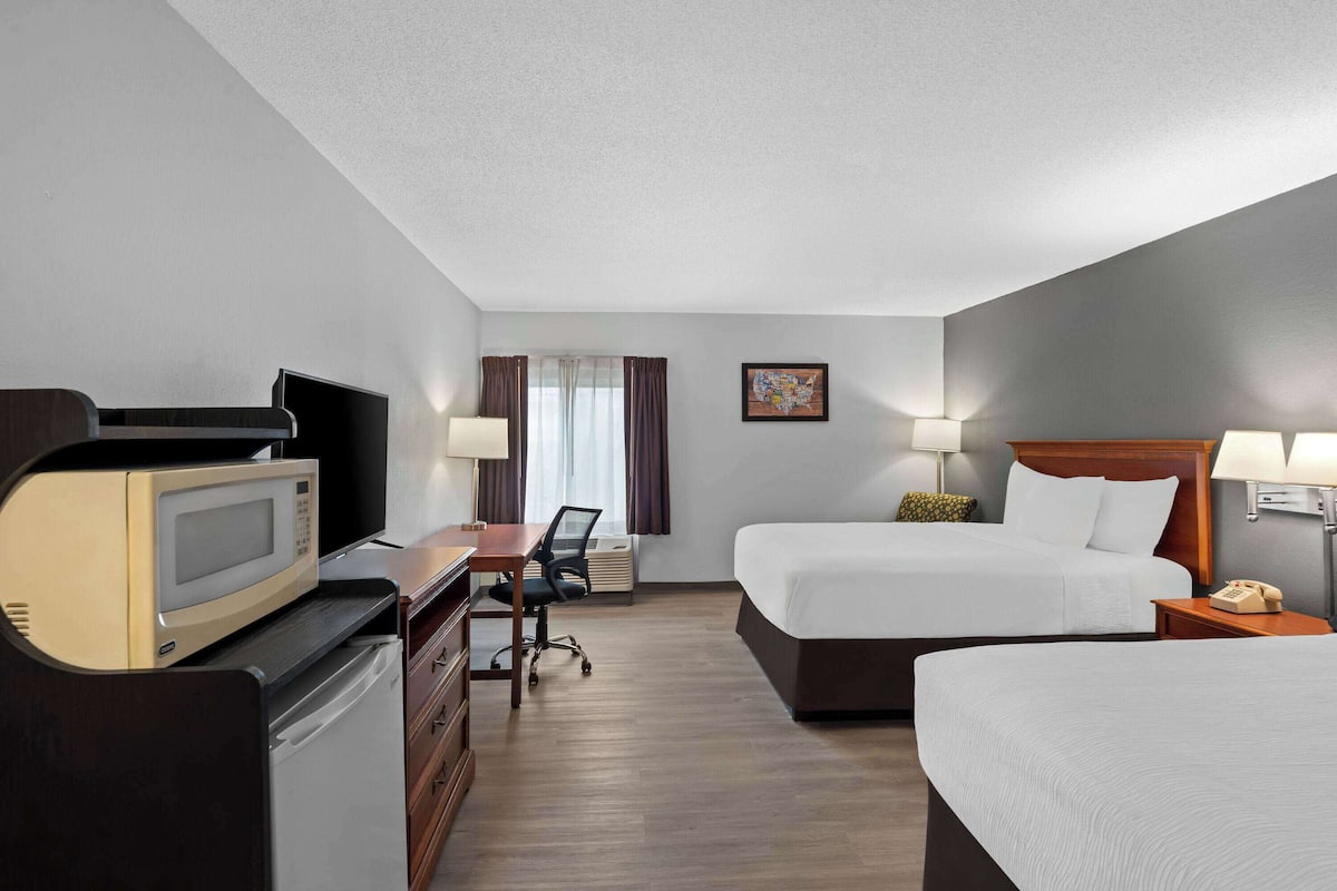 Ein Hotelzimmer mit Bett, Schreibtisch, Stuhl, Mikrowelle und Telefon.
