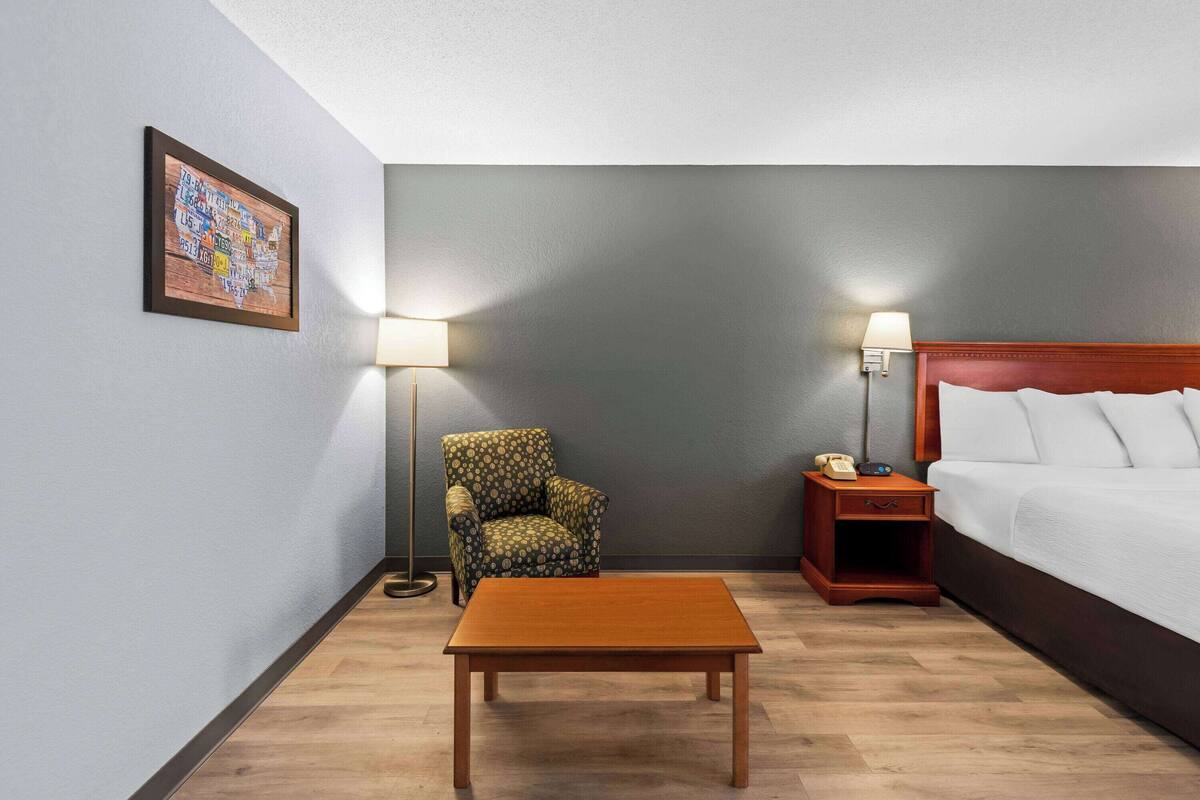 Ein Hotelzimmer mit einem Bett, einem Holztisch, einem gemusterten Sessel und zwei Nachttischlampen.