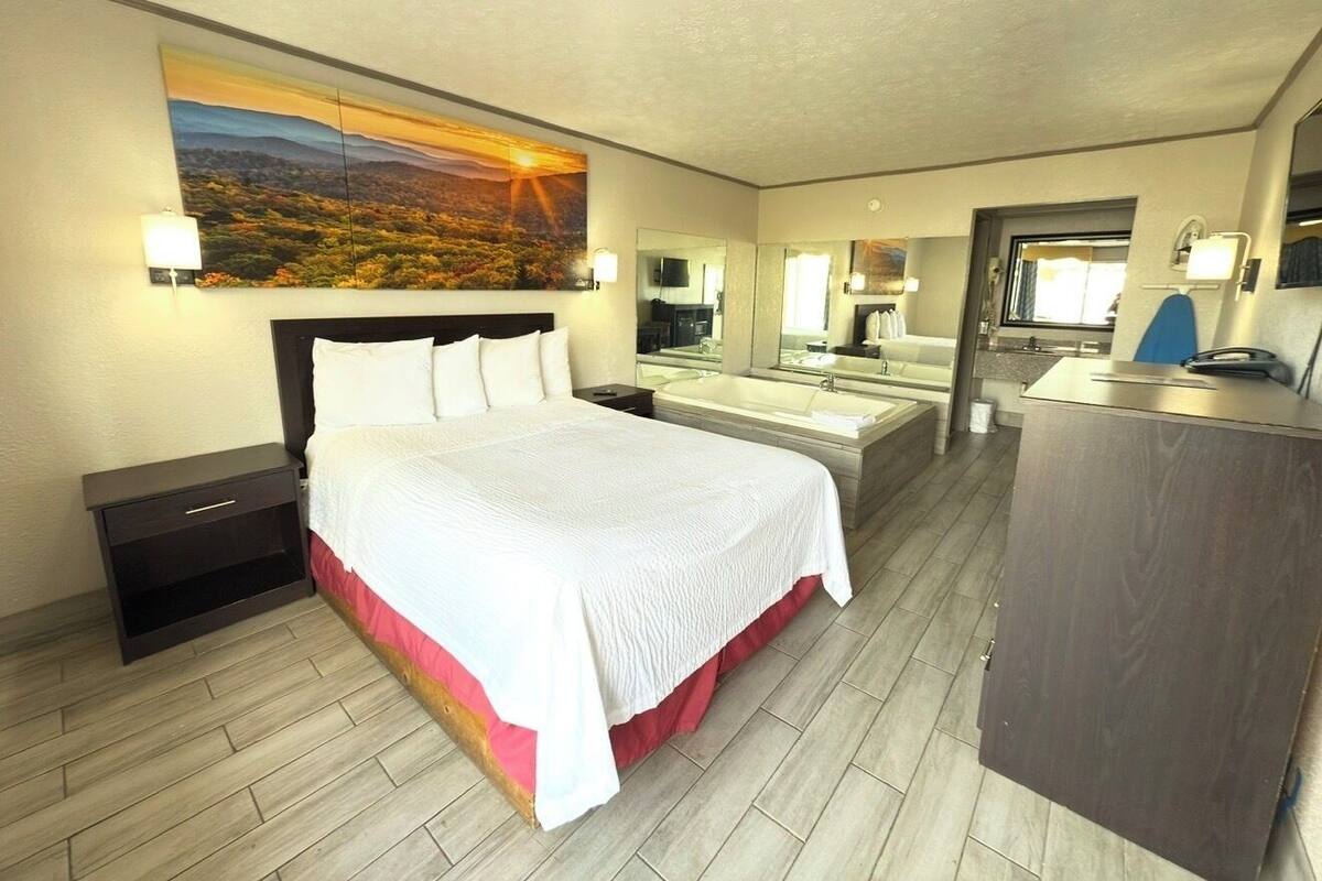 Una habitación de hotel con una cama grande, un escritorio, un espejo y un cuadro en la pared.