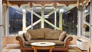 Una habitación acogedora con un sofá marrón, una mesa redonda de madera y ventanas grandes con vistas al exterior.