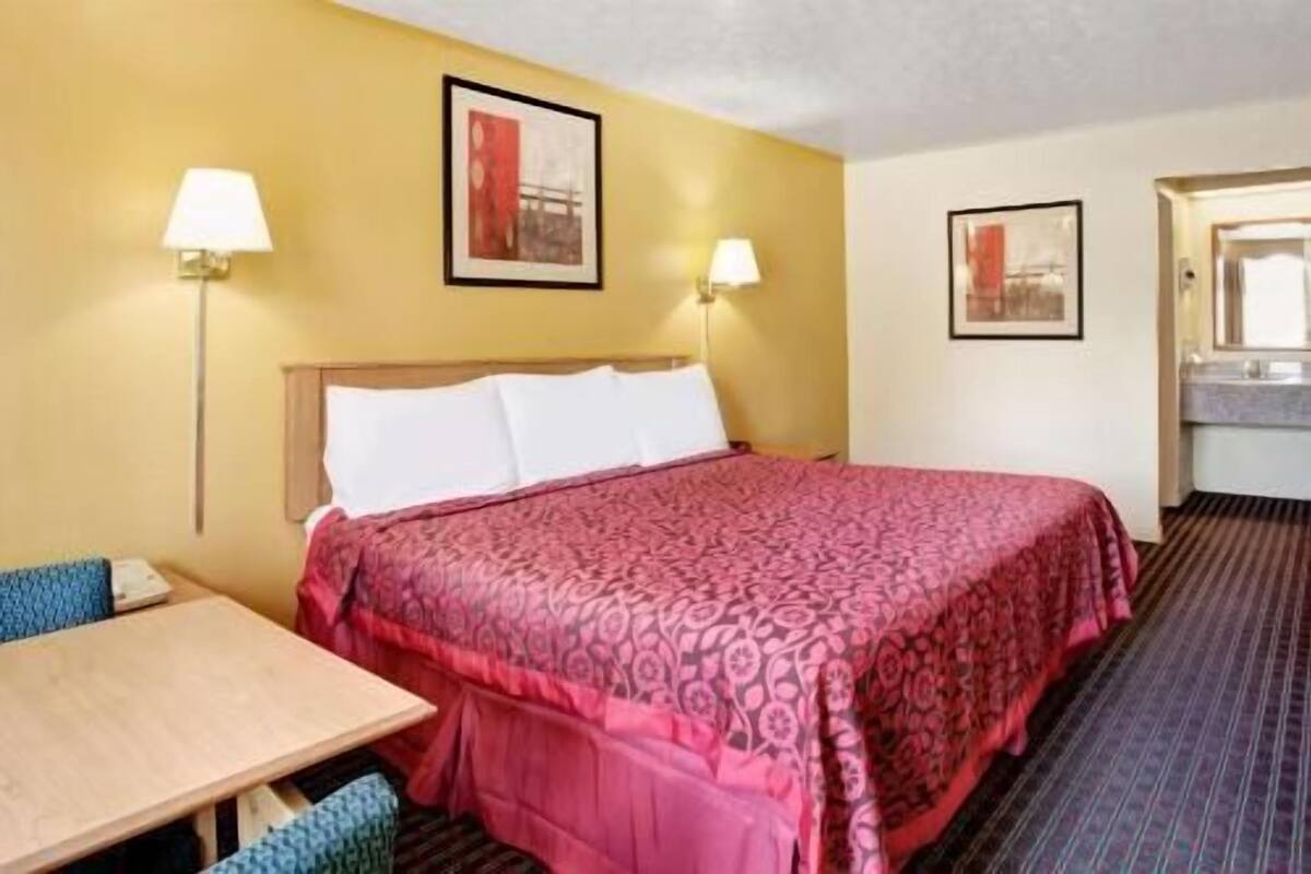 Una habitación de hotel con una cama, dos lámparas de noche, una mesa y una silla.