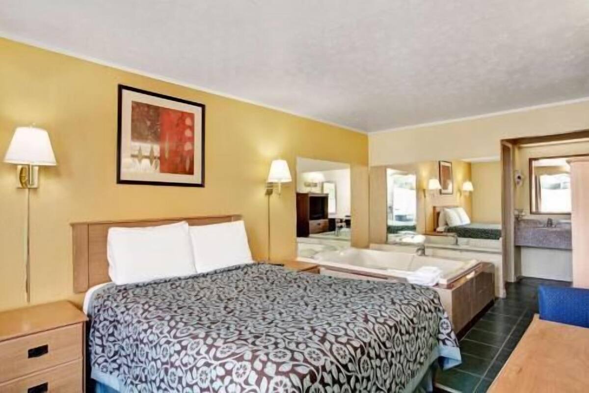 Habitación de hotel con cama, lámparas de noche, un cuadro, espejo de baño y vistas al baño.
