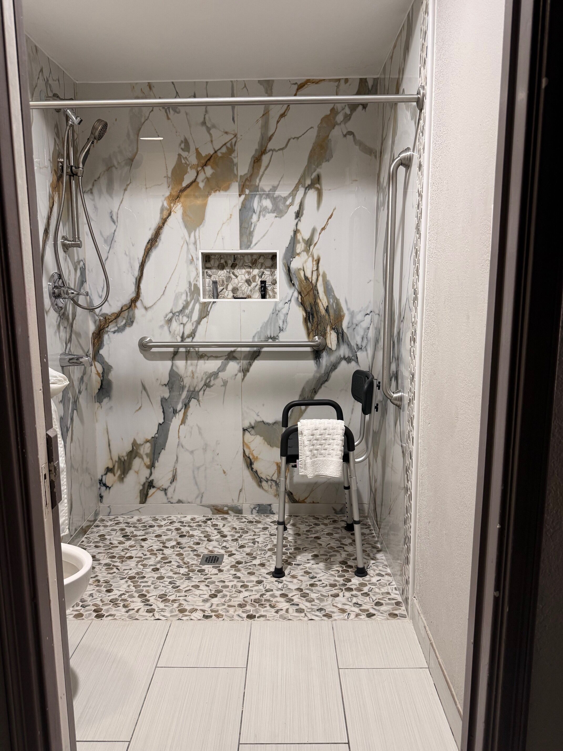 Une salle de bain moderne équipée d’une douche, d’une barre d’appui, d’un porte-serviettes et d’un fauteuil roulant.