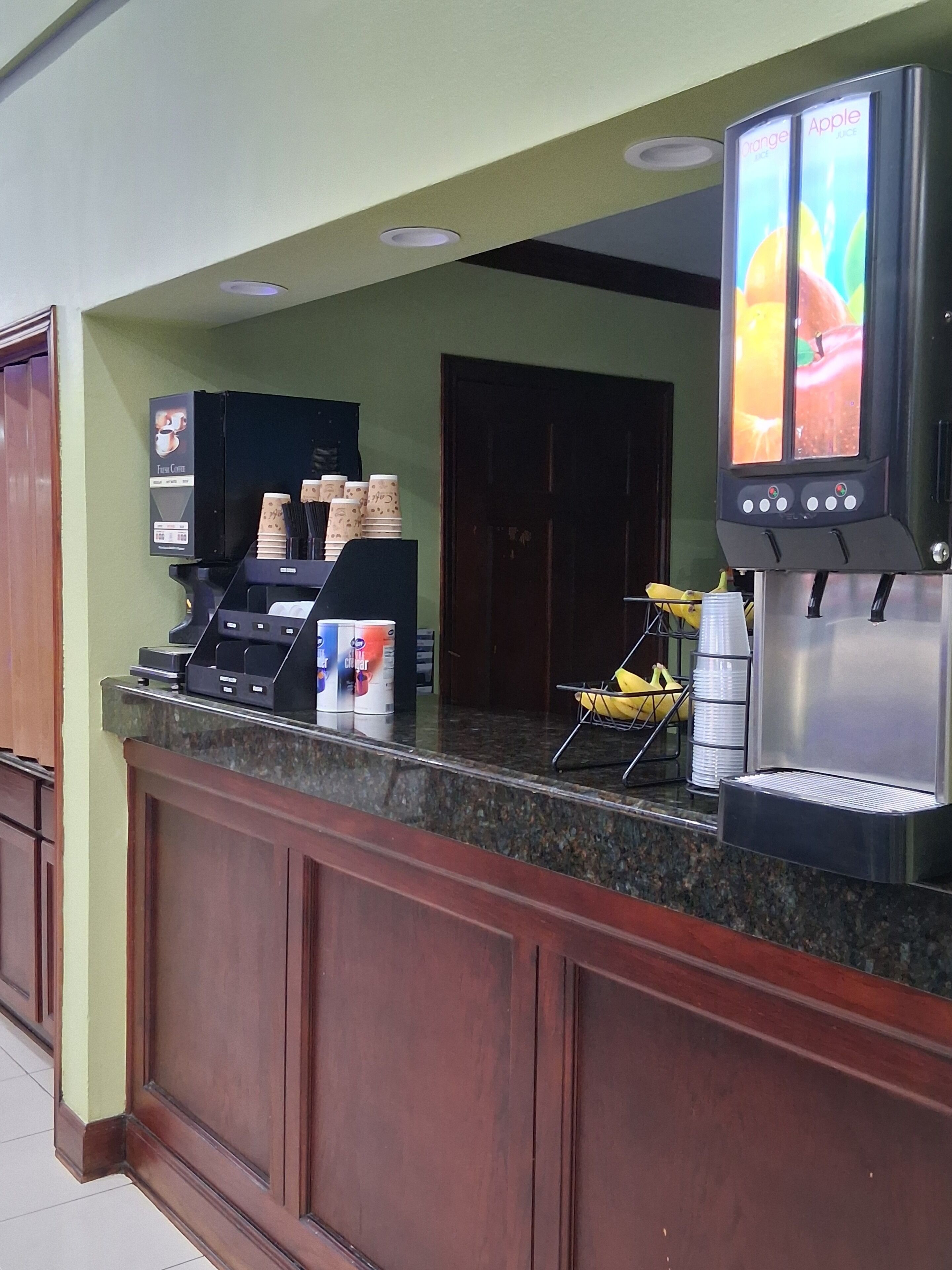 Una estación de café con dispensador de bebidas, una máquina de café y una exhibición de vasos desechables.