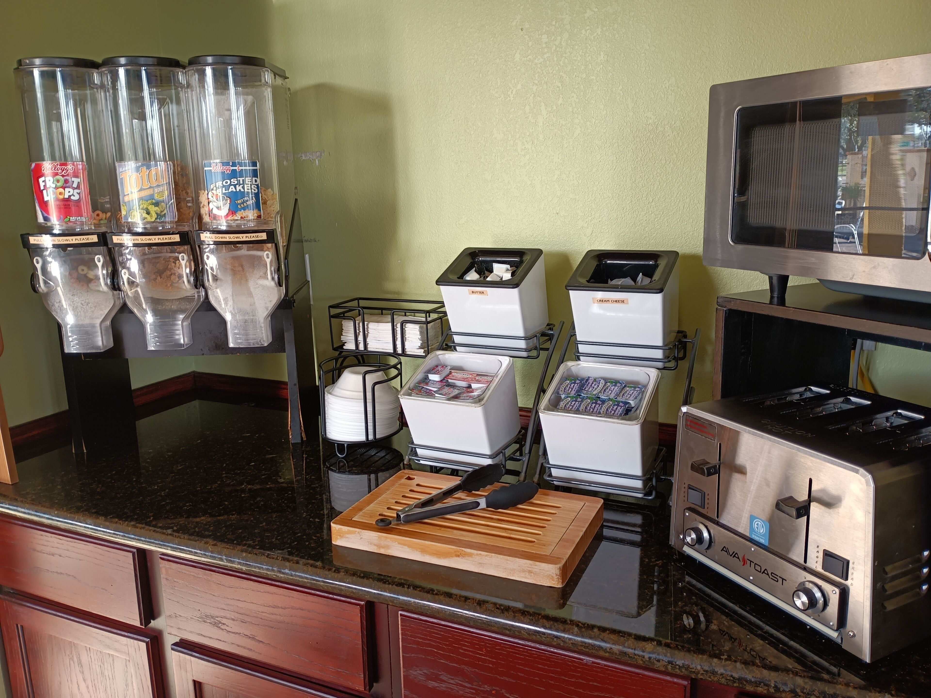 Una cocina equipada con cafetera, tostadora, microondas y tabla de cortar.