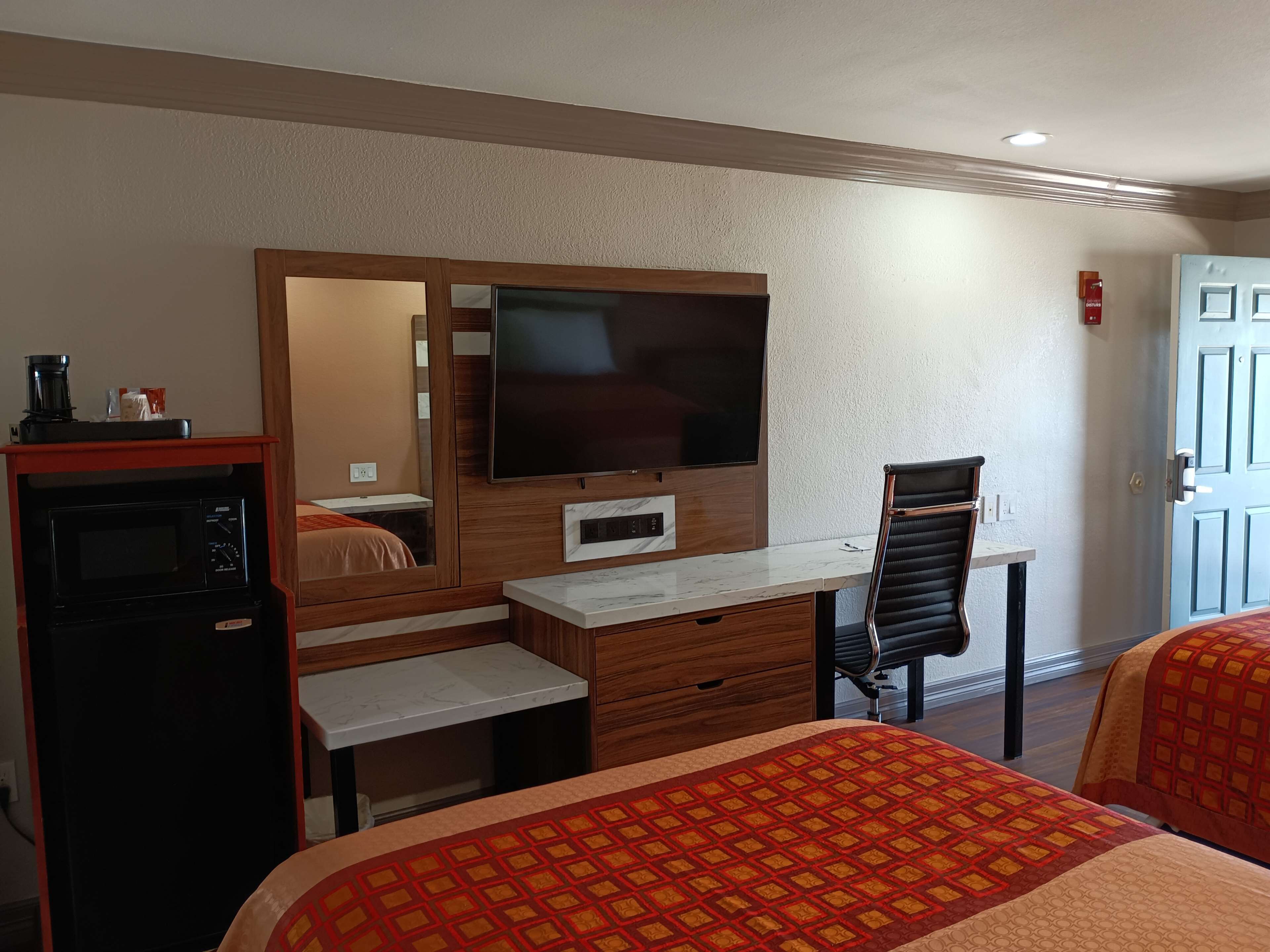 A hotel room with a bed, a desk with a chair, a television, and a microwave.