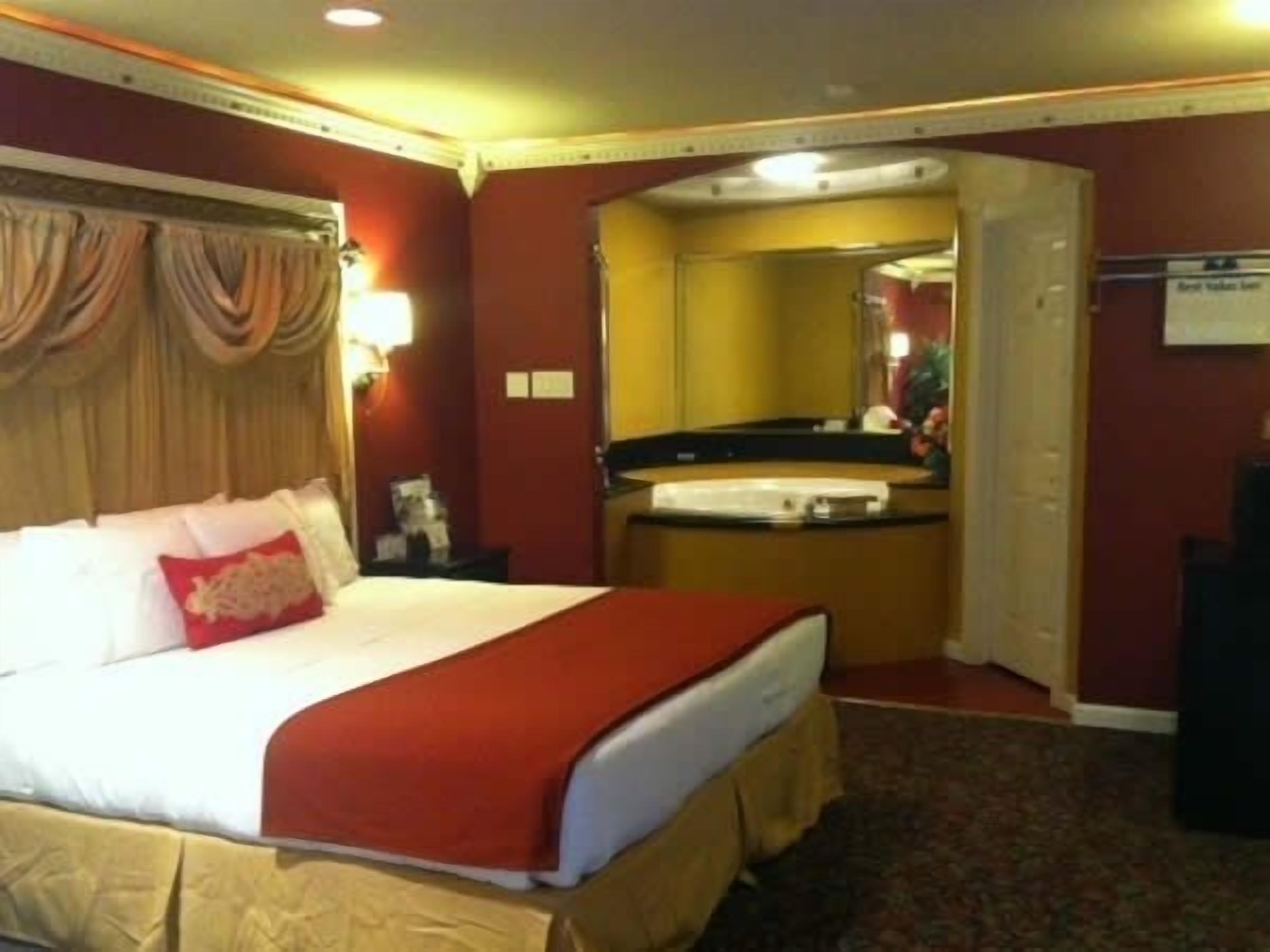 A hotel room with a large bed, a bedside table, a mirror, and a bathroom visible through an open door.