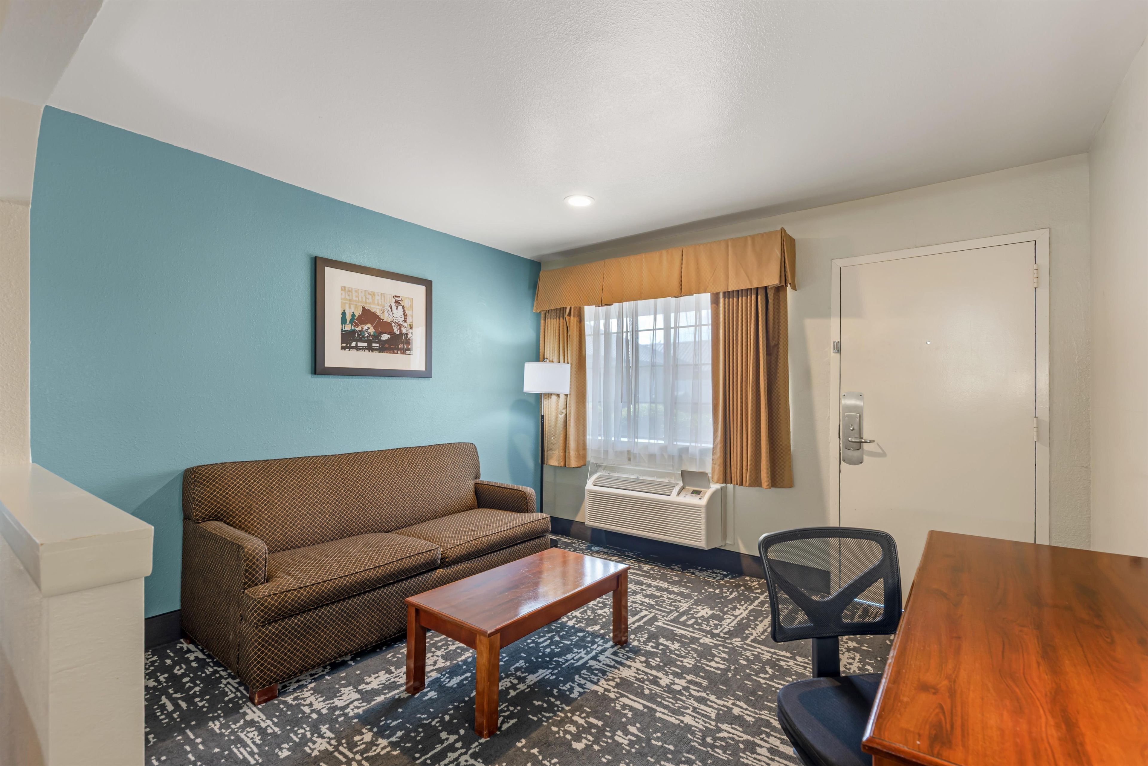 A room with a sofa, a small table, a chair, a window with curtains, and a door.