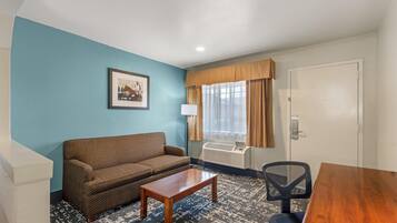 A room with a sofa, a small table, a chair, a window with curtains, and a door.