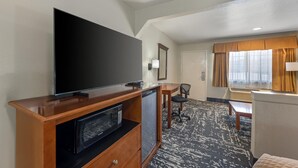A hotel room with a flat-screen TV, a microwave, a desk, a chair, and a window with curtains. - Best Western Regency Inn & Suites (Gonzales)