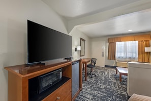 A hotel room with a flat-screen TV, a microwave, a desk, a chair, and a window with curtains. - Best Western Regency Inn & Suites (Gonzales)
