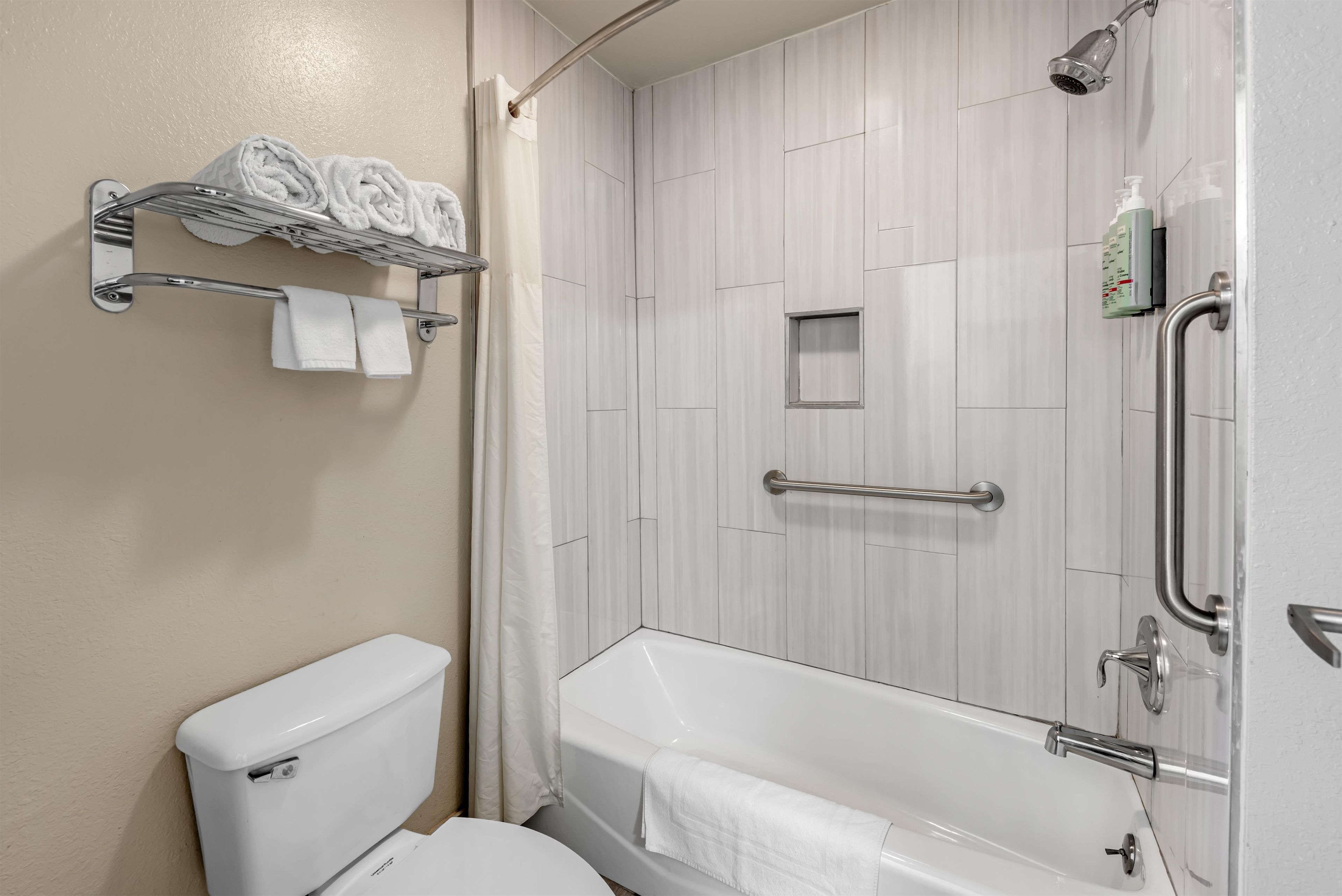 A bathroom with a toilet, a shower with a grab bar, and a towel rack with towels.