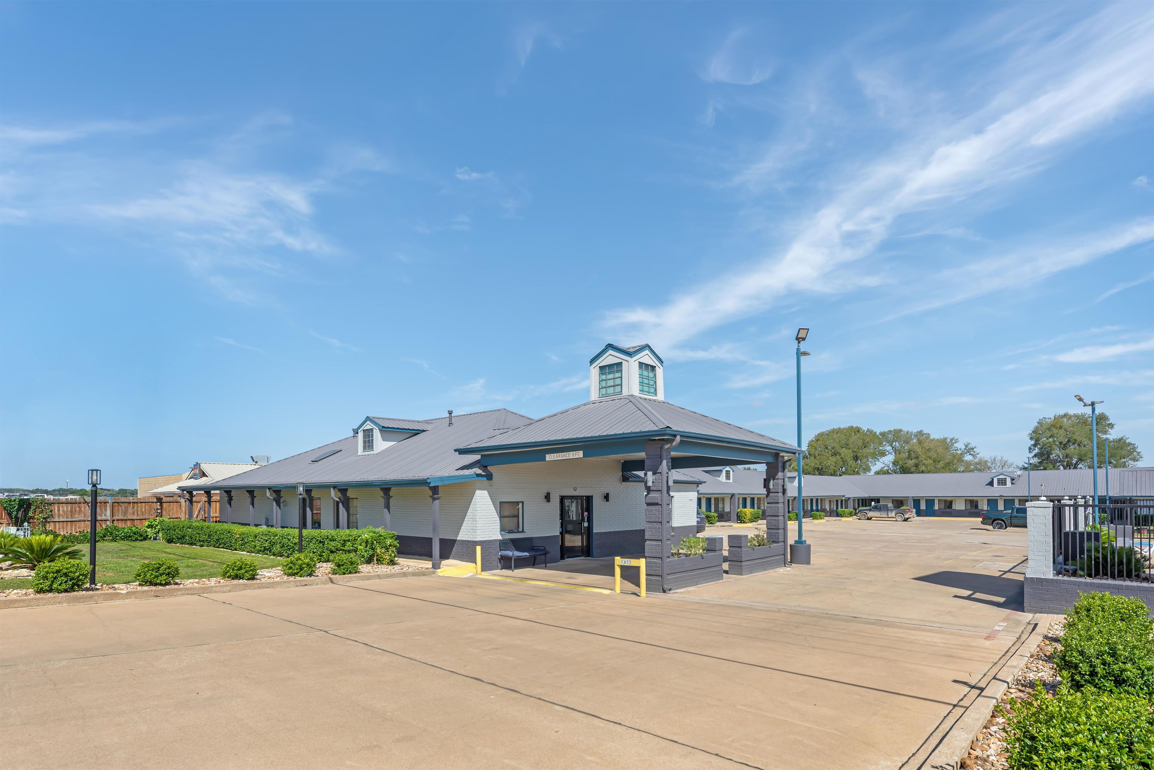 A motel with a covered parking area, a clear sky, and a fenced property.