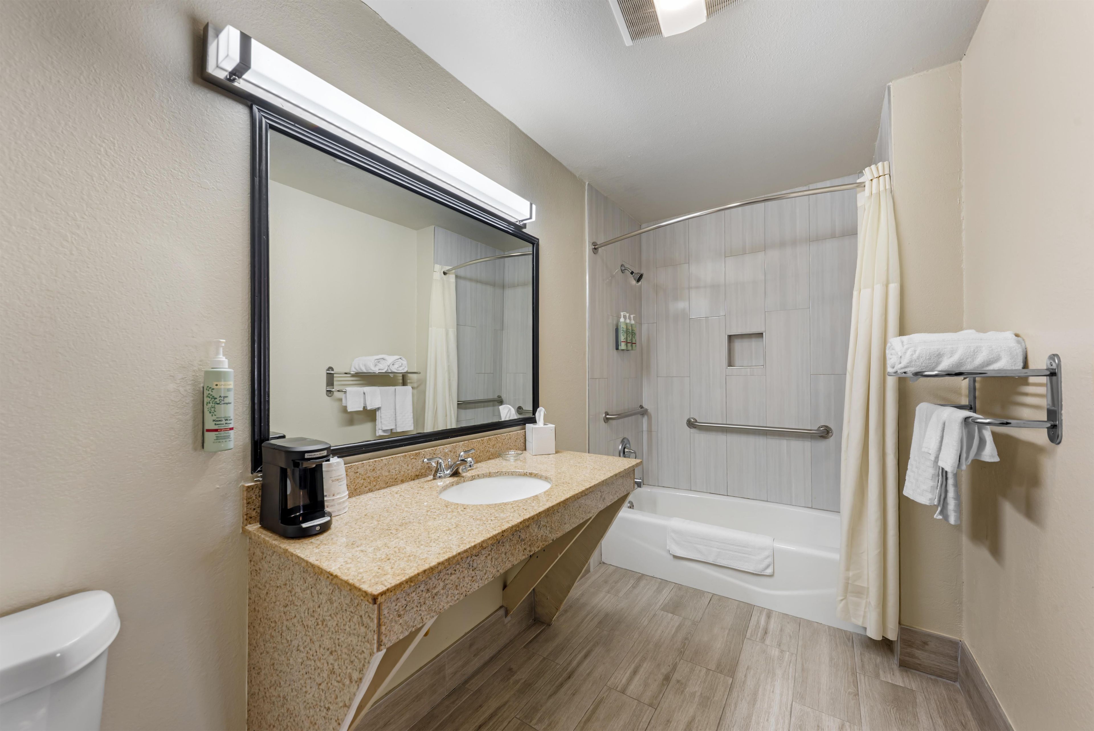 A hotel bathroom with a sink, mirror, shower, and toilet.