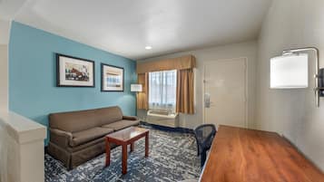 Une chambre d’hôtel avec un canapé, une petite table, un bureau, une lampe et une fenêtre avec des rideaux.