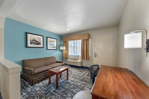 Habitación de hotel con sofá, una mesita, escritorio, lámpara y ventana con cortinas.