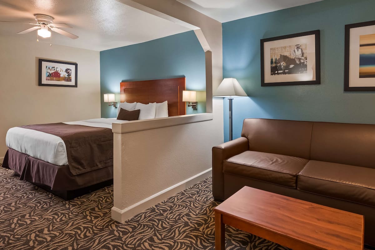 A hotel room with a bed, a sofa, a coffee table, a desk, and a ceiling fan.