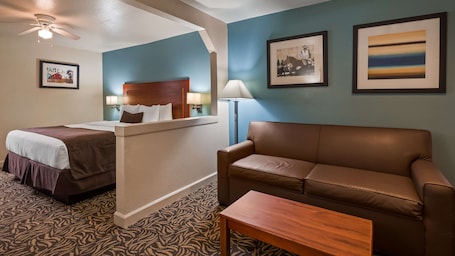 A hotel room with a bed, a sofa, a coffee table, a desk, and a ceiling fan.