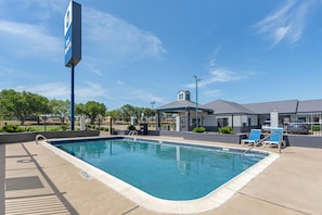A clear swimming pool with a lifeguard stand, lounge chairs, and a covered area with a roof. - Best Western Regency Inn & Suites (Gonzales)