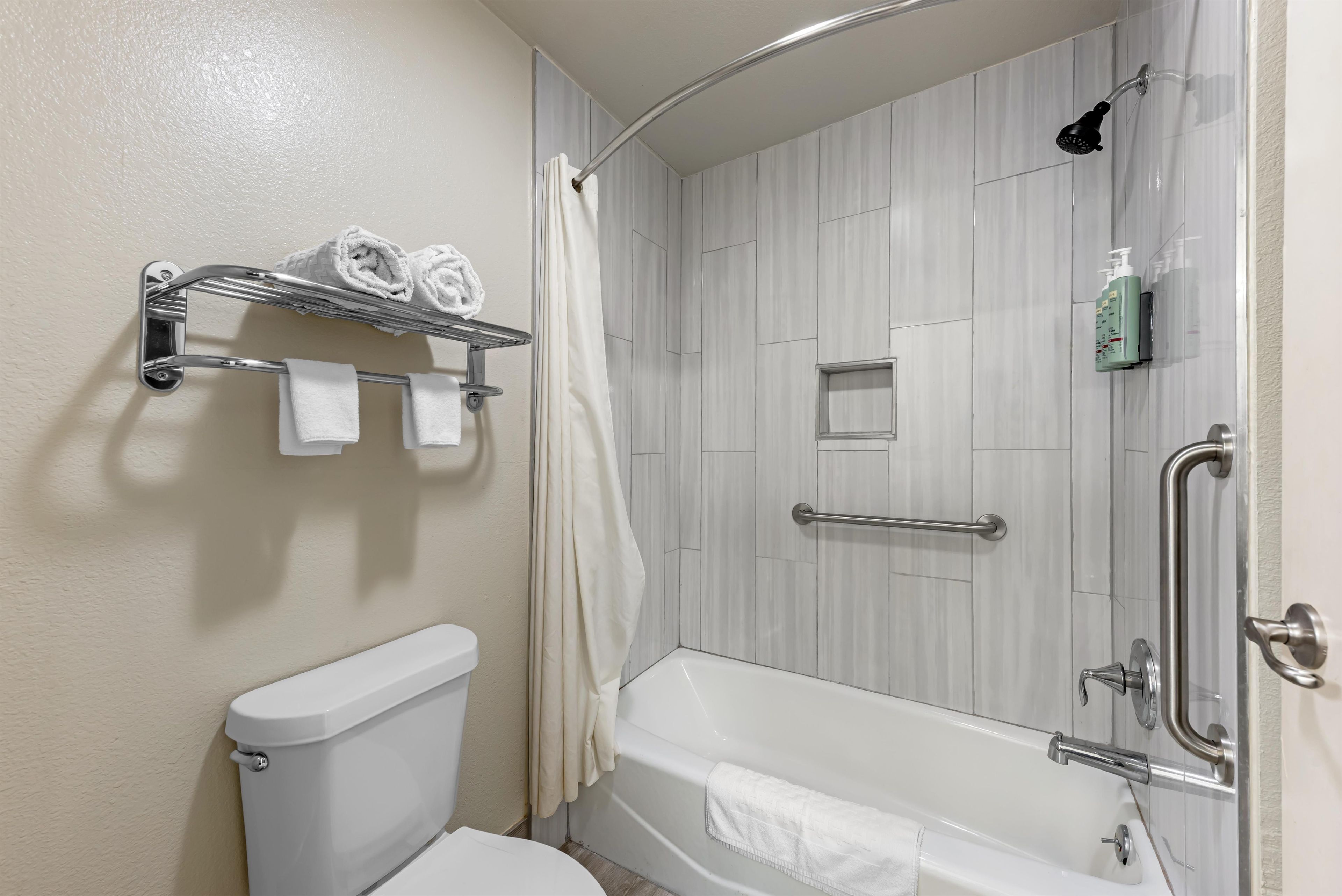 Un baño con inodoro, ducha con puerta de vidrio y bañera. Hay toallas en un estante y una cortina de ducha.