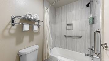 Un baño con inodoro, ducha con puerta de vidrio y bañera. Hay toallas en un estante y una cortina de ducha.