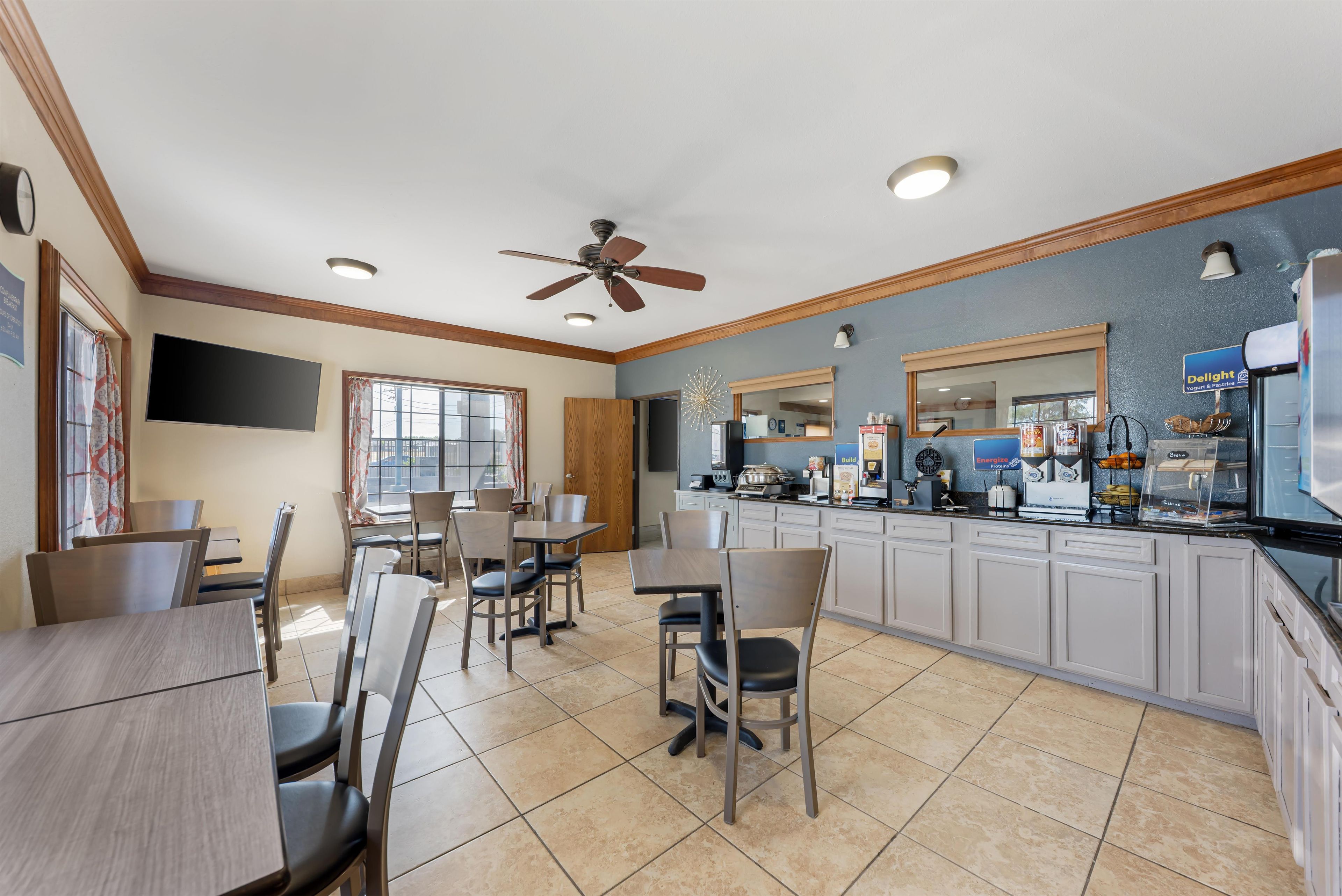 A dining area with tables and chairs, a kitchen counter with food items, and a ceiling fan.