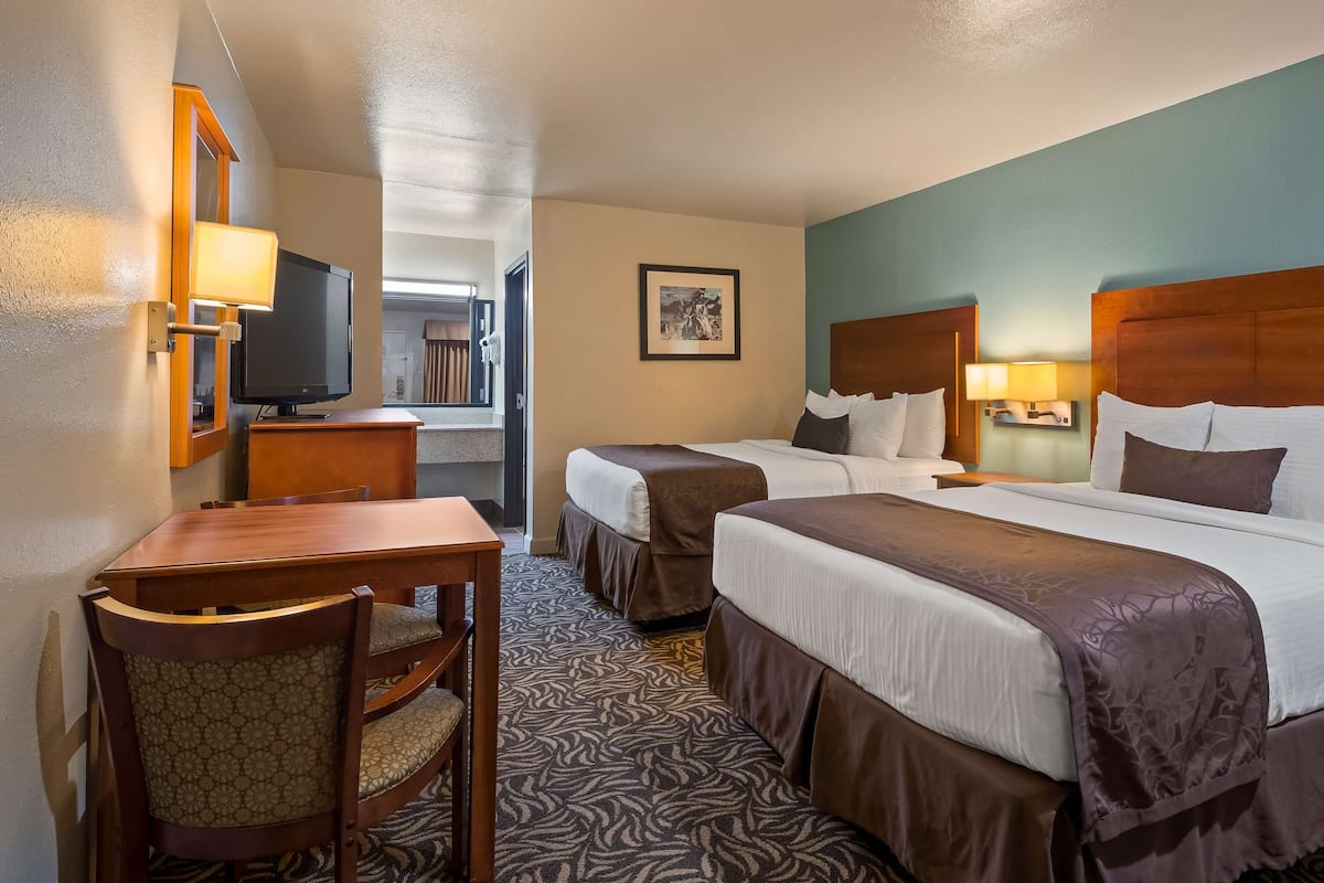 A hotel room with two beds, a desk, a chair, a television, and a framed picture on the wall.