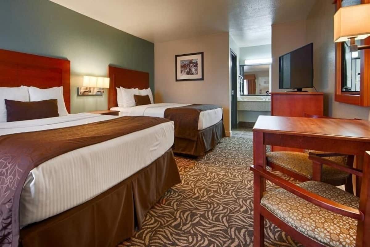 A hotel room with two beds, a desk, a chair, a television, and a bathroom visible in the background.