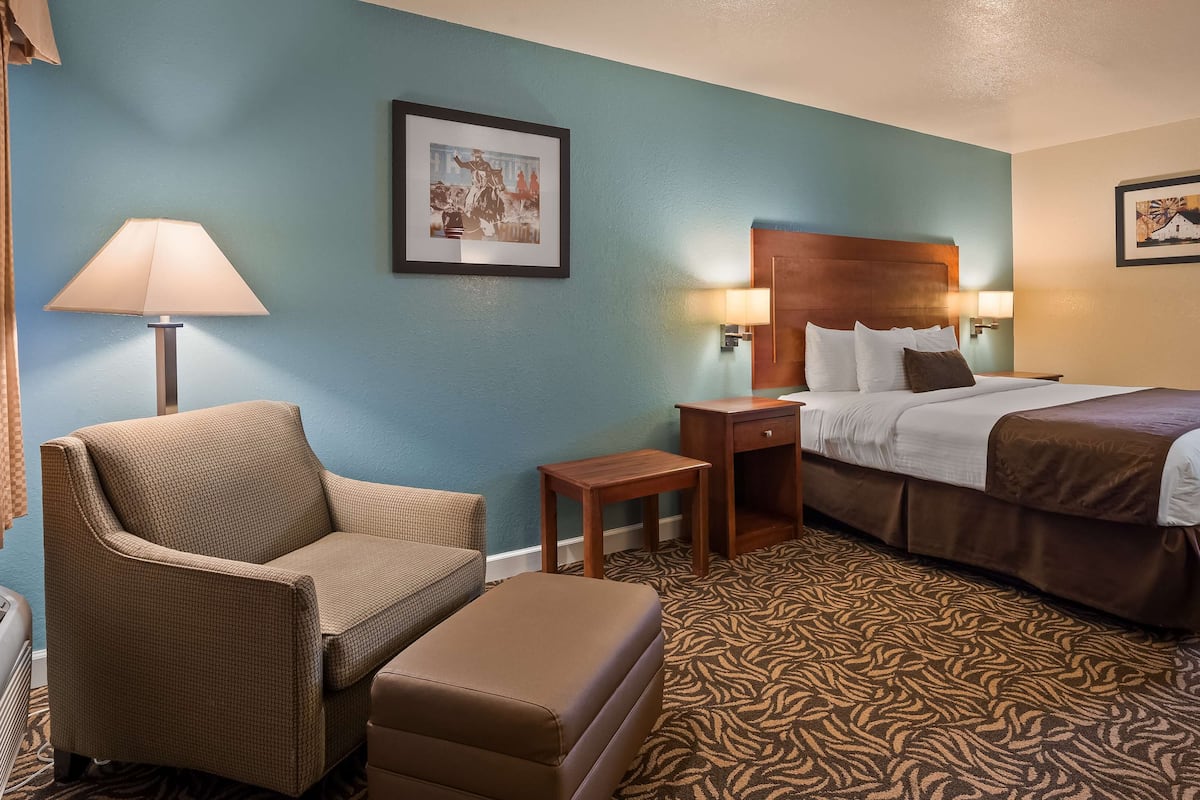 A hotel room with a bed, a chair, a nightstand, a lamp, and two framed pictures on the walls.